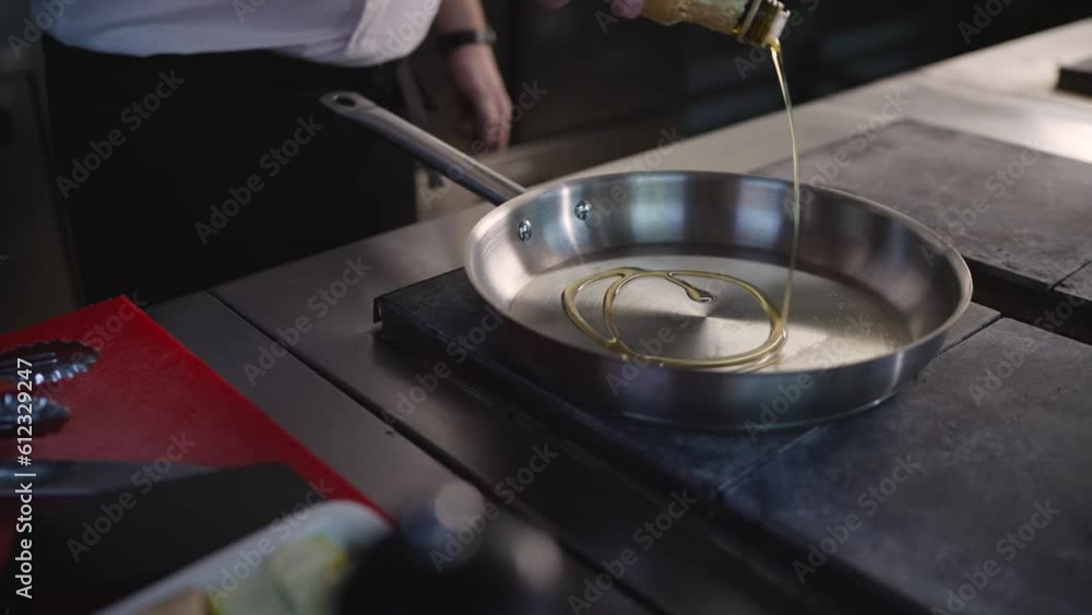 The chef pours oil into a hot pan in a professional kitchen cooking in a restaurant. Close-up of a cook pouring oil into a frying pan. The chef pours oil into a hot pan in a professional kitchen cooking in a restaurant. Close-up of a cook pouring oil into a frying pan.