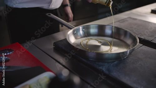 The chef pours oil into a hot pan in a professional kitchen cooking in a restaurant. Close-up of a cook pouring oil into a frying pan. photo