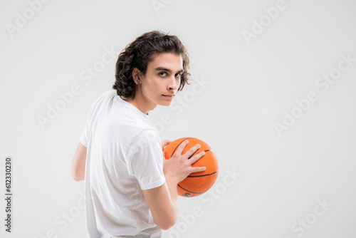 Smiling teenager, basketball player posing with a ball in his hand on a white background.