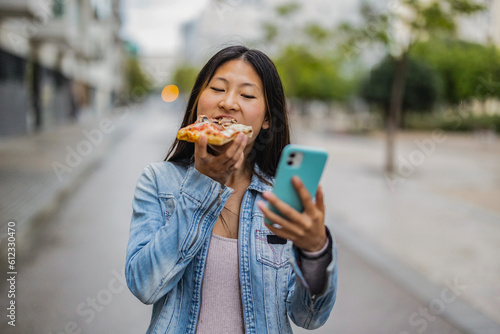 Foto asian woman on the street eating pizza while checking social media with smart ph