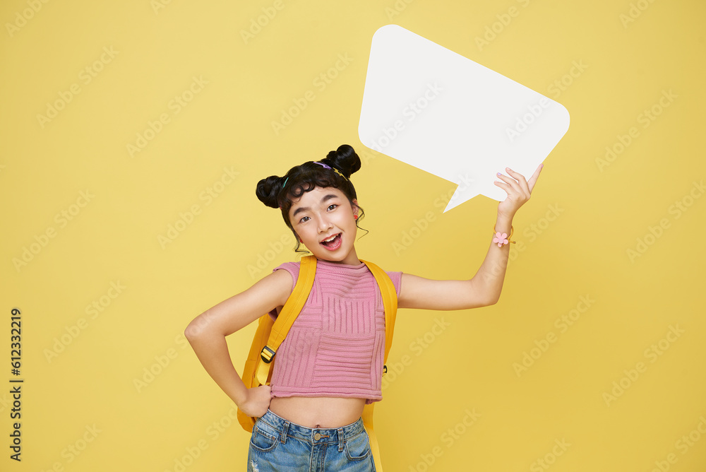 Happy smiling Asian girl student holding up an empty white speech bubble isolated on yellow studio background. Happy smiling Asian girl student holding up an empty white speech bubble isolated on yellow studio background.