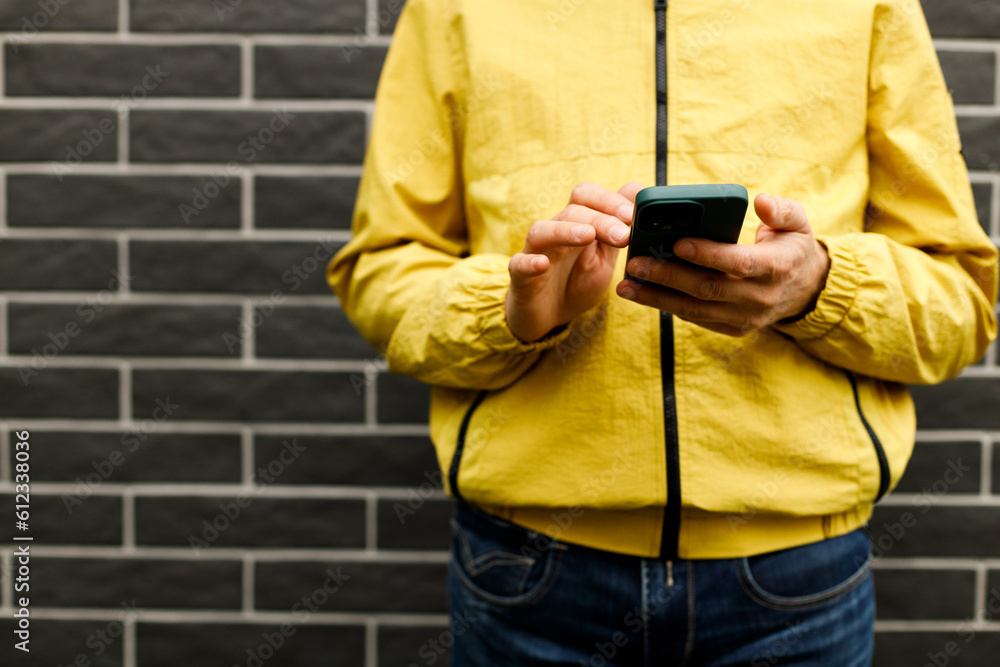 Fototapeta premium Man in yellow raincoat standing on the street with mobile phone and wireless earphones