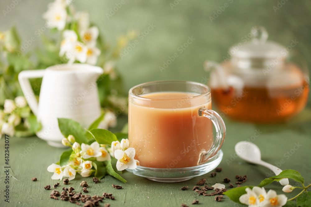 Composition with cup of jasmine milk tea and flowers on green background Composition with cup of jasmine milk tea and flowers on green background