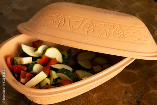 Classic roman pot full of zucchini, aubergine and paprika ready to bake. Healthy ancient cooking style in a clay pot.