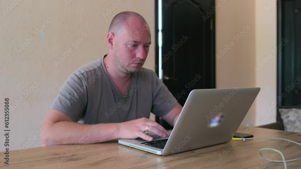 Focused caucasian man working at laptop tensely thinks about his task. IT specialist, programmer work in home office. Remote work arrangements. Focused caucasian man working at laptop tensely thinks about his task. IT specialist, programmer work in home office. Remote work arrangements.