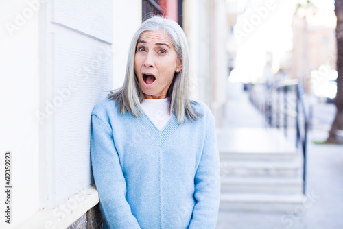 senior retired pretty white hair woman looking very shocked or surprised, staring with open mouth saying wow