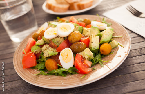 dish of fresh vegetables arugula, avocado, cherry tomatoes with olives and quail eggs on dining table