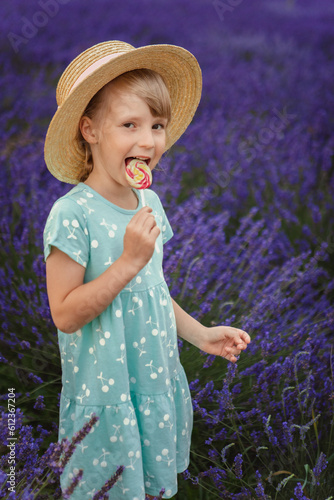 A little girl in a straw hat eats a lollipop in a lavender field