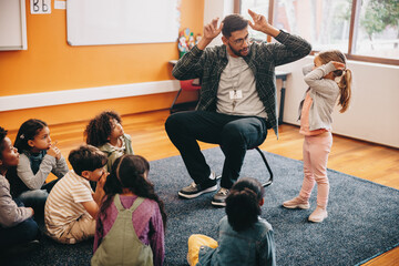 Male educator in a primary school class. Teacher shows a little girl how to do heads and shoulders
