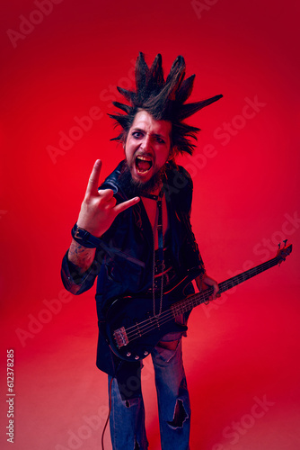Aggressive impressive pose. Rok musician  man posing with hand gesture on rock against red studio background in neon light. Concept of music  lifestyle  subculture  art  youth  human emotions