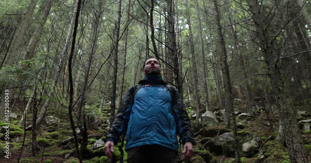 Portrait of a man with a backpack standing in the rain in the forest and raising his hands to the mountain breathing in the mountain air and meditating. The man is alone in the mountains. Hiking among Portrait of a man with a backpack standing in the rain in the forest and raising his hands to the mountain breathing in the mountain air and meditating. The man is alone in the mountains. Hiking among