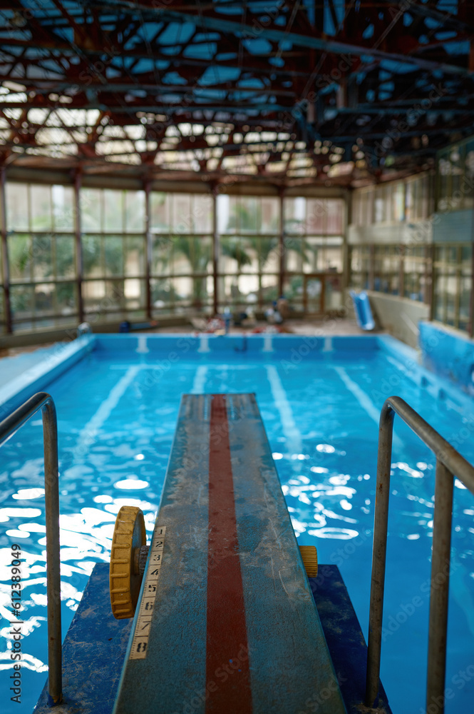 Diving board at empty swimming pool with reflections of light in water