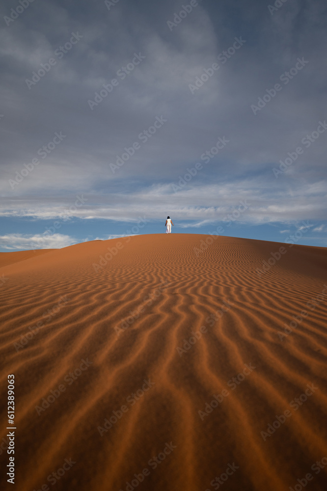 Stunning view of a tourist walking on a sand dune in Merzouga, Morocco.