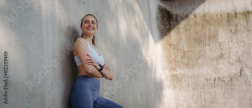 Fototapeta Naklejka Na Ścianę i Meble -  Portrait of young sporty woman in sportswear leaning agaist concrete wall in the city.