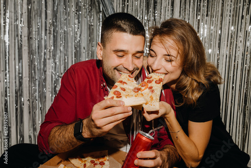 Portrait of a happy couple. They laugh  eat pizza and have a good time against the background of silver rain