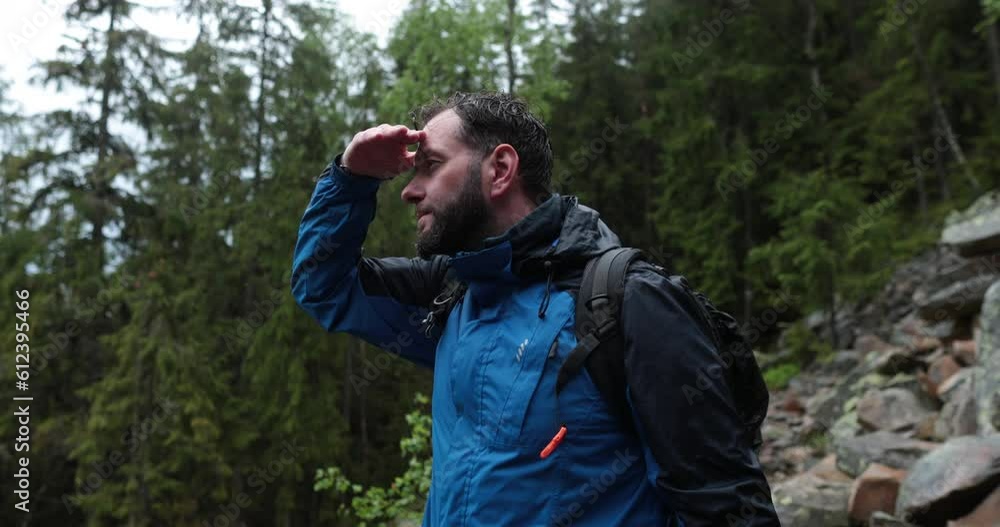 A male tourist with a backpack is standing on large stones. A close-up tourist looks at the landscape in rainy weather. Backpack walking in the mountains on stones in the rain. A male tourist with a backpack is standing on large stones. A close-up tourist looks at the landscape in rainy weather. Backpack walking in the mountains on stones in the rain.