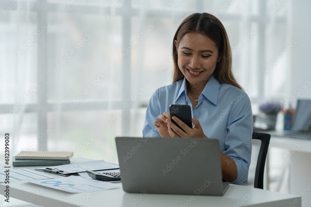 Happy Asian businesswoman talking on the phone and smiling while sitting at work using smartphone to talk. Contact via online application, concept of management Happy Asian businesswoman talking on the phone and smiling while sitting at work using smartphone to talk. Contact via online application, concept of management