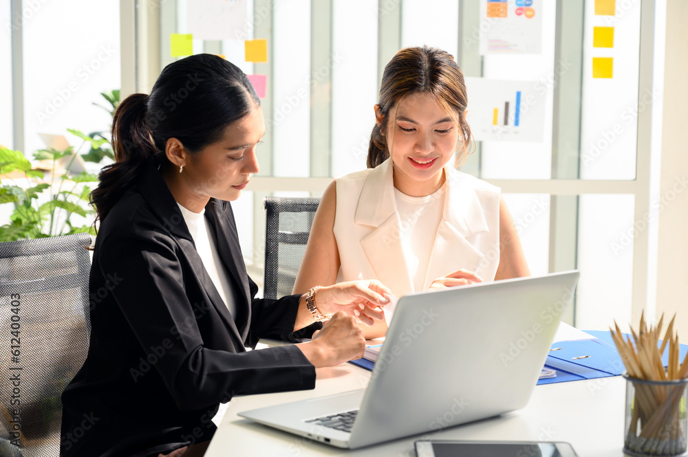 Two young Asian businesswoman in smart casuals read some documents, making plans together. Business people talking together with documents at office. Two young Asian businesswoman in smart casuals read some documents, making plans together. Business people talking together with documents at office.