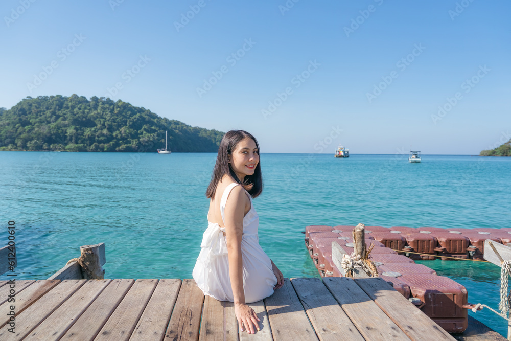 Happy asian woman sitting on wooden pier among tropical sea in summer vacation
