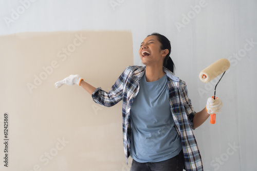 Canvas Print Young asian woman enjoying renovation time at home while holding roller