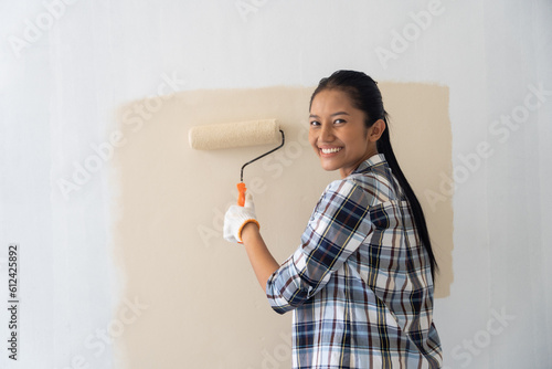Young asian woman enjoying renovation time at home while holding roller. Repair and remodeling concept