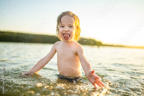 Cute toddler boy playing by a lake on hot summer day. Adorable child having fun outdoors during summer vacations.