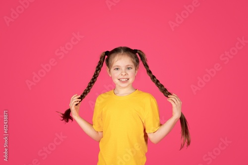 Portrait of cute cheerful little girl with braids posing over pink background,