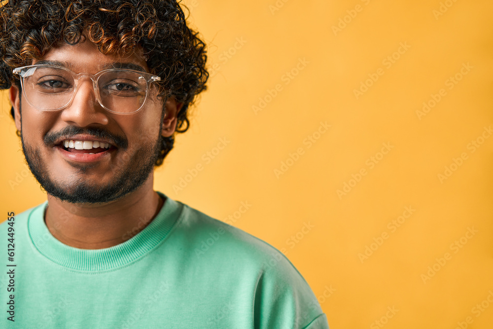 Cropped portrait of a handsome curly-haired Indian man in a turquoise t-shirt and glasses smiling and looking at the camera. Cropped portrait of a handsome curly-haired Indian man in a turquoise t-shirt and glasses smiling and looking at the camera.