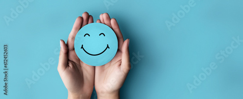 Fototapeta Naklejka Na Ścianę i Meble -  Promoting Positive Mental Health: Hand Holding Blue Paper Cut Happy Smile Face for World Mental Health Day