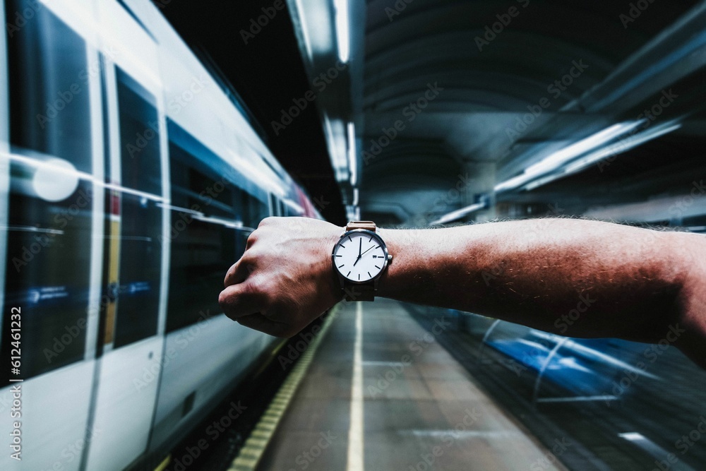 Man holding up his wristwatch with a train passing in the blurry background in the subway