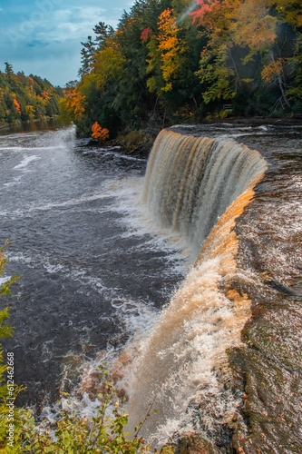 Vertical of the mesmerizing Tahquamenon Falls waterfall in Michigan surrounded by autumn foliage photo