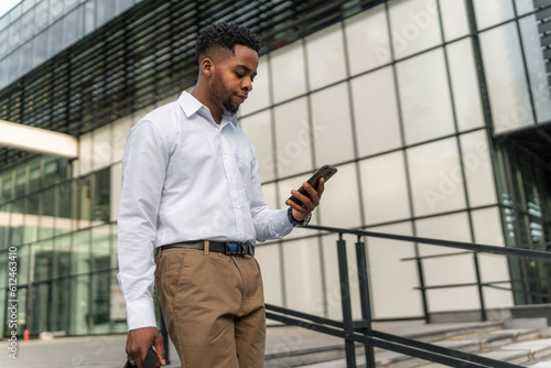 With purpose in his stride, the stylish African-American businessman carries his laptop bag and holds his phone, ready to conquer the day's challenges.