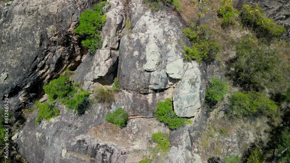 Aerial slow movement around cliff surrounded by dense trees in 4K