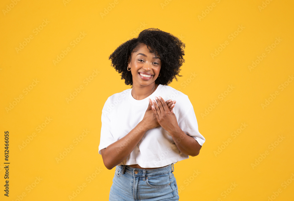 Glad millennial african american curly woman in white t-shirt put hands to chest, heart, enjoy good news Glad millennial african american curly woman in white t-shirt put hands to chest, heart, enjoy good news
