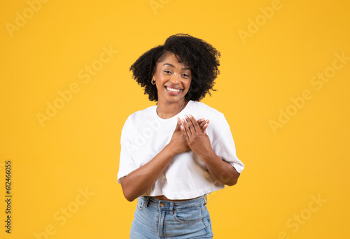 Glad millennial african american curly woman in white t-shirt put hands to chest, heart, enjoy good news