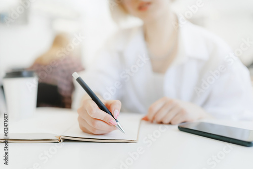 Influencer blogger woman writes content plan in notepad in cafe with coffee, white light