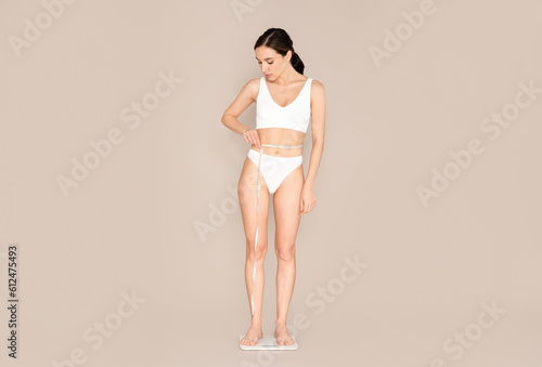 Slim young woman checking weight and measuring waist © Prostock-studio