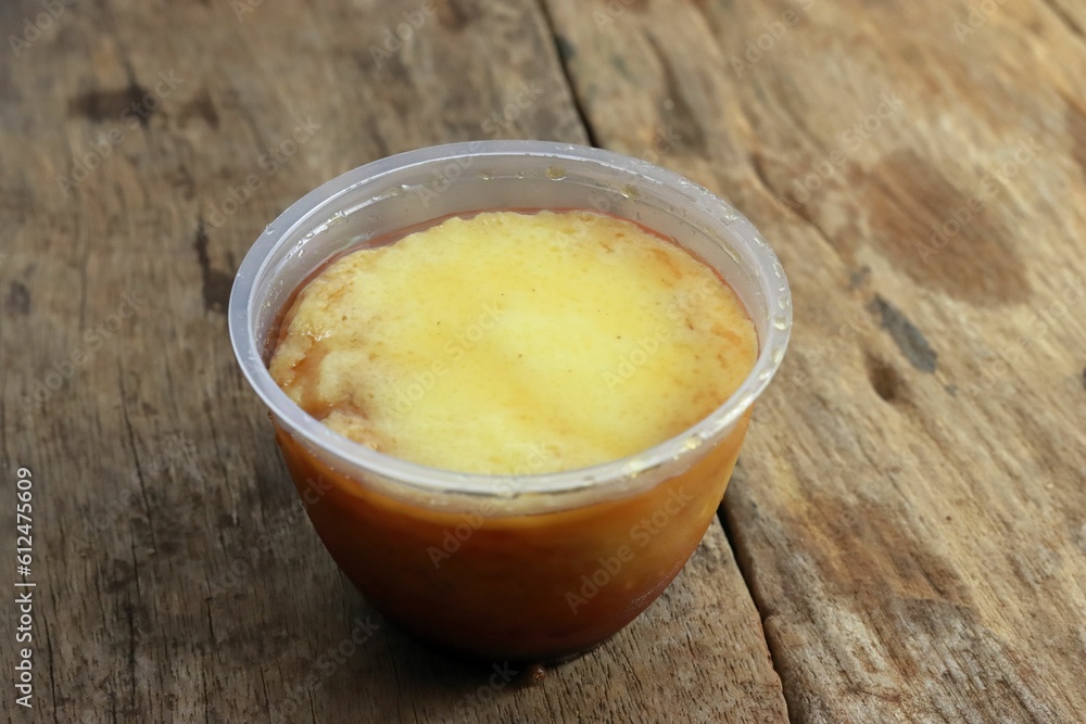 Closeup shot of homemade orange and yellow pudding in a plastic container on wooden background Closeup shot of homemade orange and yellow pudding in a plastic container on wooden background