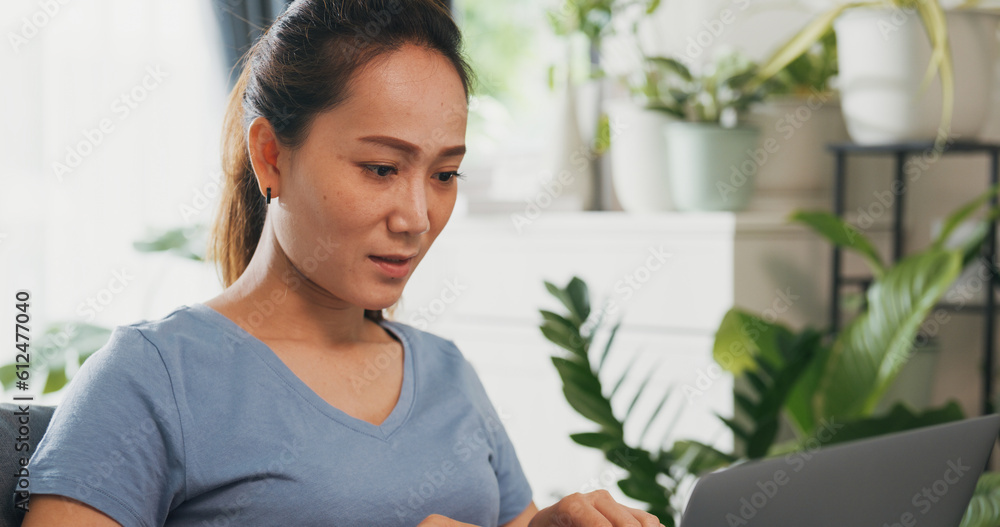 Young Asian woman wear casual calm sitting on wing chair use laptop computer thinking the idea for working full of plants in living room greenhouse. Coronavirus and stay home, Work from home concept. Young Asian woman wear casual calm sitting on wing chair use laptop computer thinking the idea for working full of plants in living room greenhouse. Coronavirus and stay home, Work from home concept.