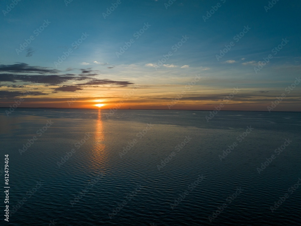 Lovely aerial view of a golden sun shining brightly down on a dark blue sea before sunset