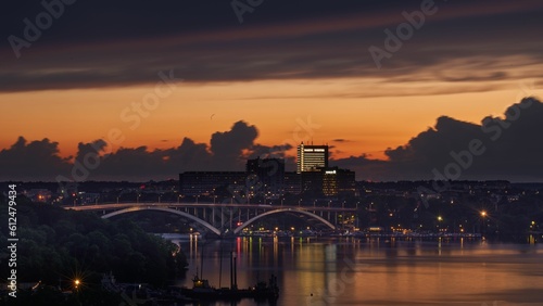 Beautiful view of a dark orange cloudy sky over a river surrounded by modern buildings at sunset