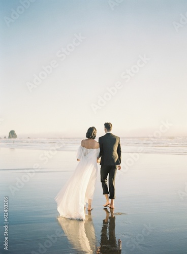Beautiful vertical back shot of a newly wed couple walking barefoot on the beach