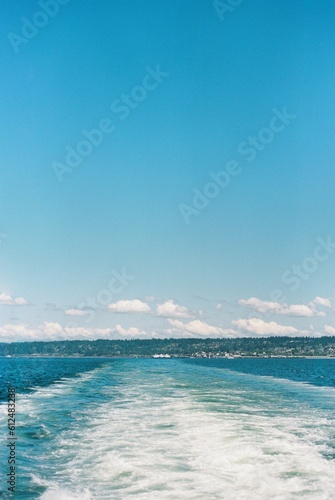 Vertical shot of a boat trail in the sea and the clear blue sky with landscape in the distance