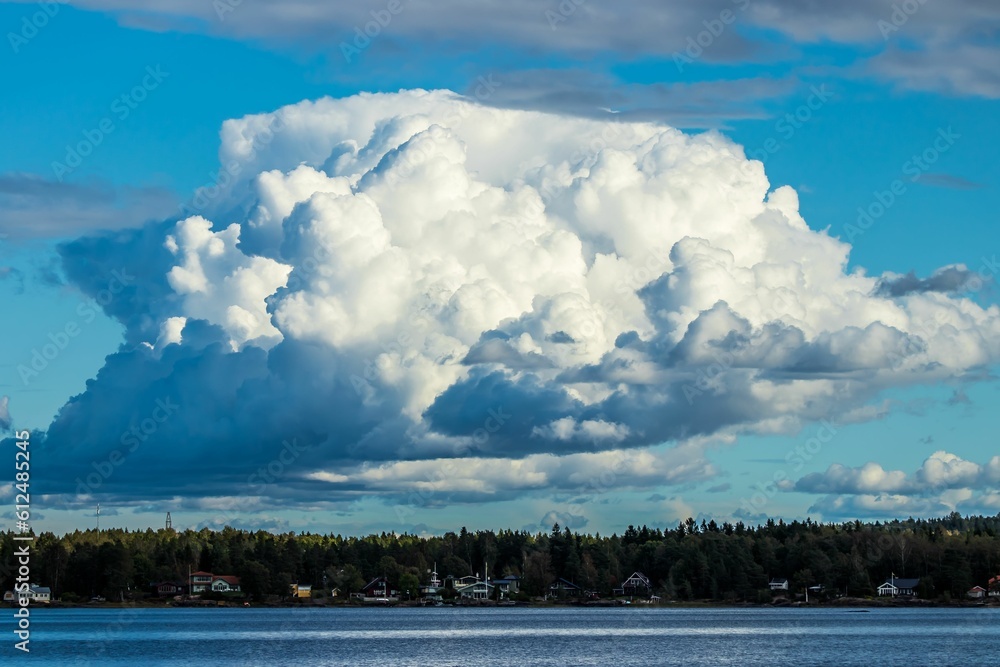 Huge cumulus cloud hanging over a silent blue lake bordered by a line of thick trees on a sunny day Huge cumulus cloud hanging over a silent blue lake bordered by a line of thick trees on a sunny day