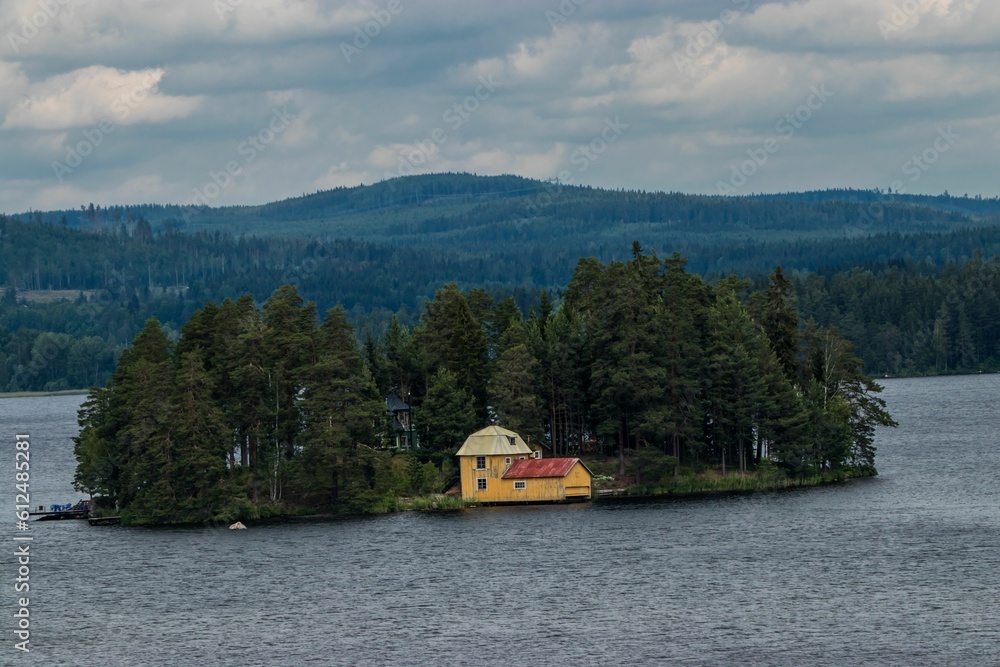 Beautiful view of a small island on a lake surrounded by vast hills covered by dark trees