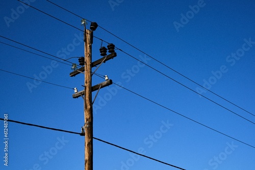Low angle shot of a electric pole with wires on a background of blue sky