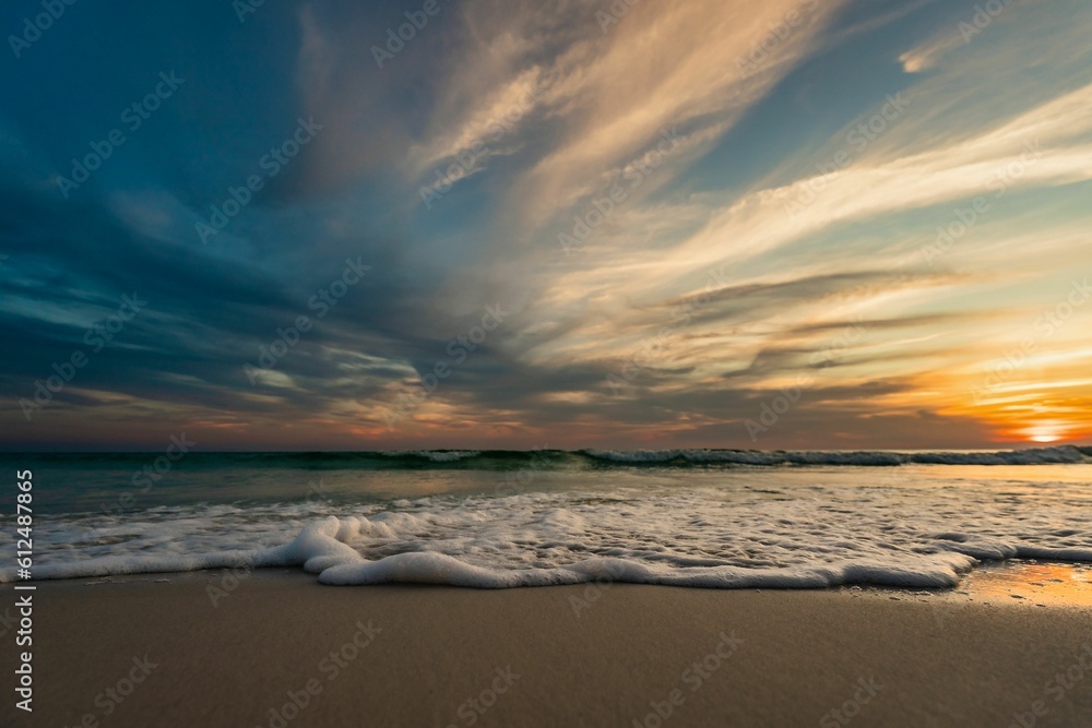 Tranquil scenery of a sandy beach with clouds and sunset in the background