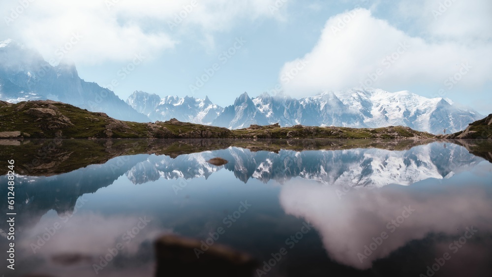 Scenic view of a calm reflective lake surrounded by snow-covered mountains under the cloudy sky