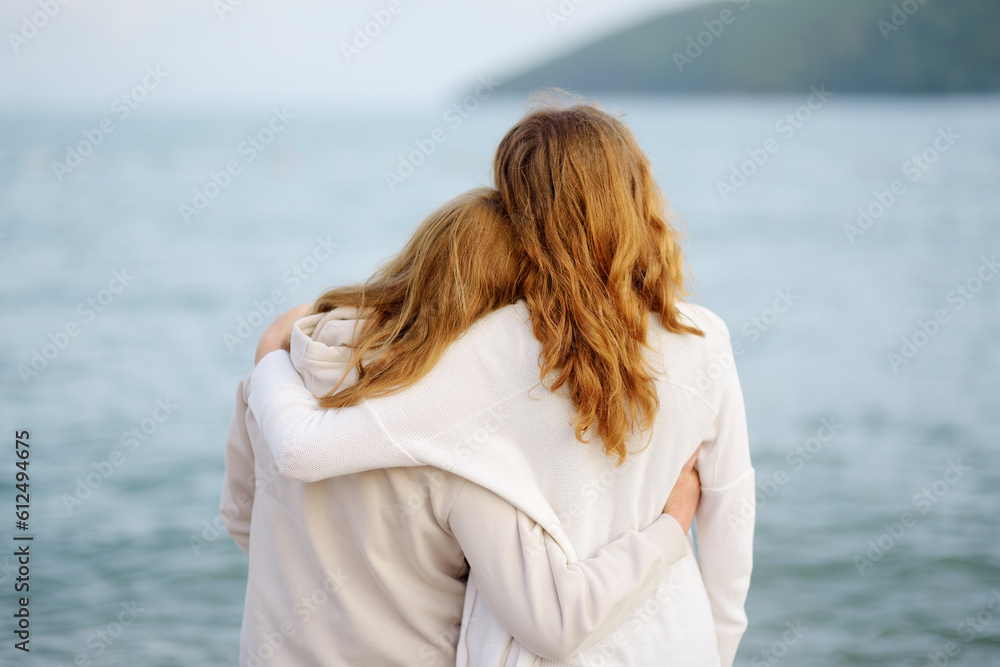 Redhead senior mother and her adult beautiful daughter are walking together on the sea shore. Redhead senior mother and her adult beautiful daughter are walking together on the sea shore.