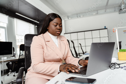 Young african american woman in business suit using laptop at office